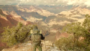 A man with a hiking backpack and poles walking towards the Grand Canyon.